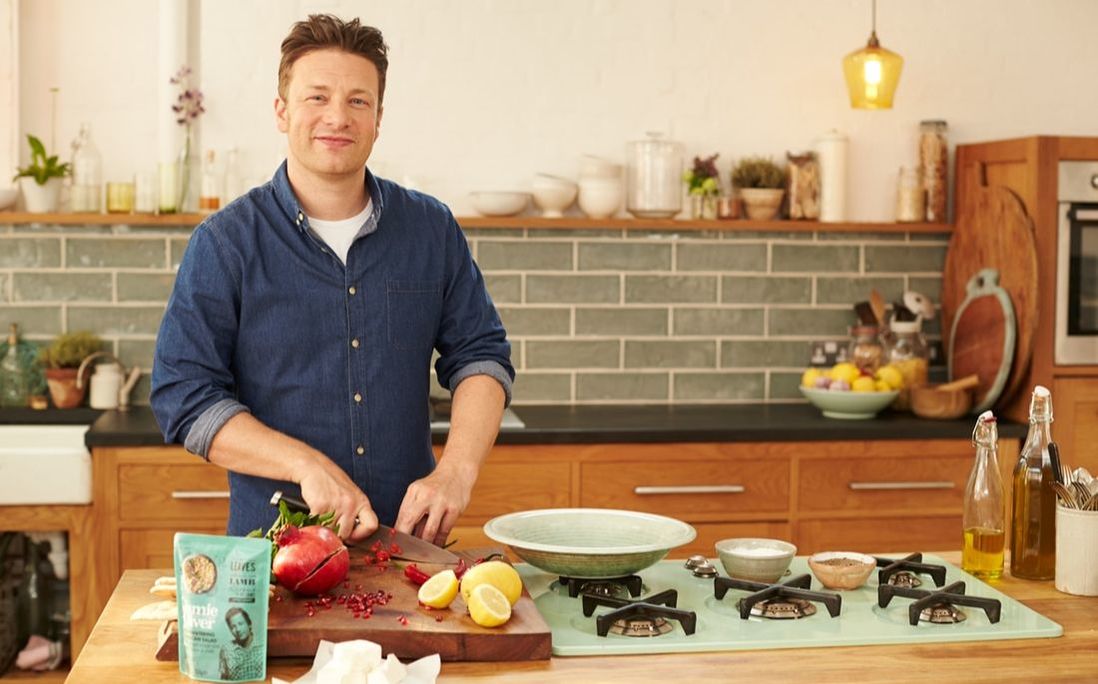 Jamie Oliver in the kitchen slicing tomatoes. grains